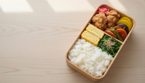 A bright overhead shot of a single, beautifully arranged traditional Japanese bento box on a wooden table (