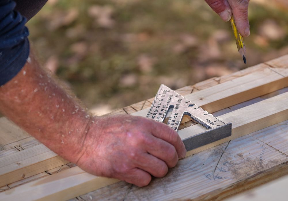 A picture of a man using a speed square on lumber material. 