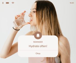 A woman drinking a glass of water upon a water drinking schedule reminder.